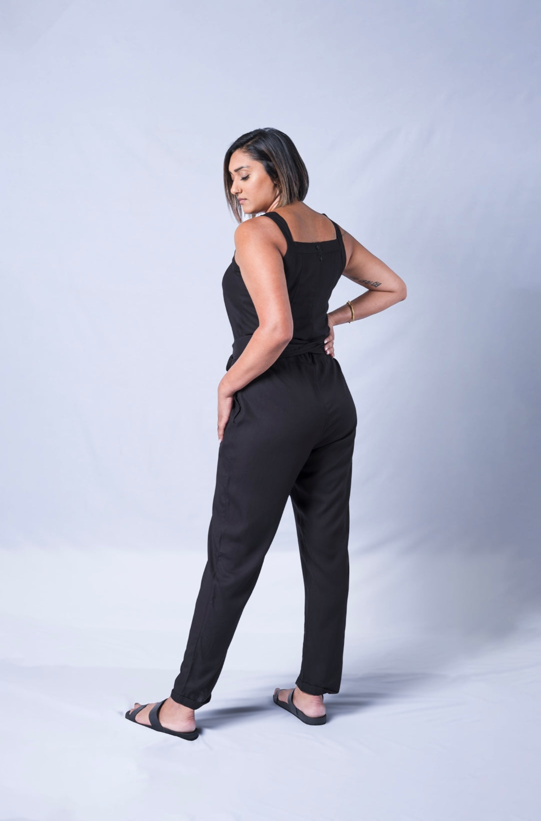 All In One Jumpsuit Model Standing showing back of the jumpsuit. Waistband tied to front