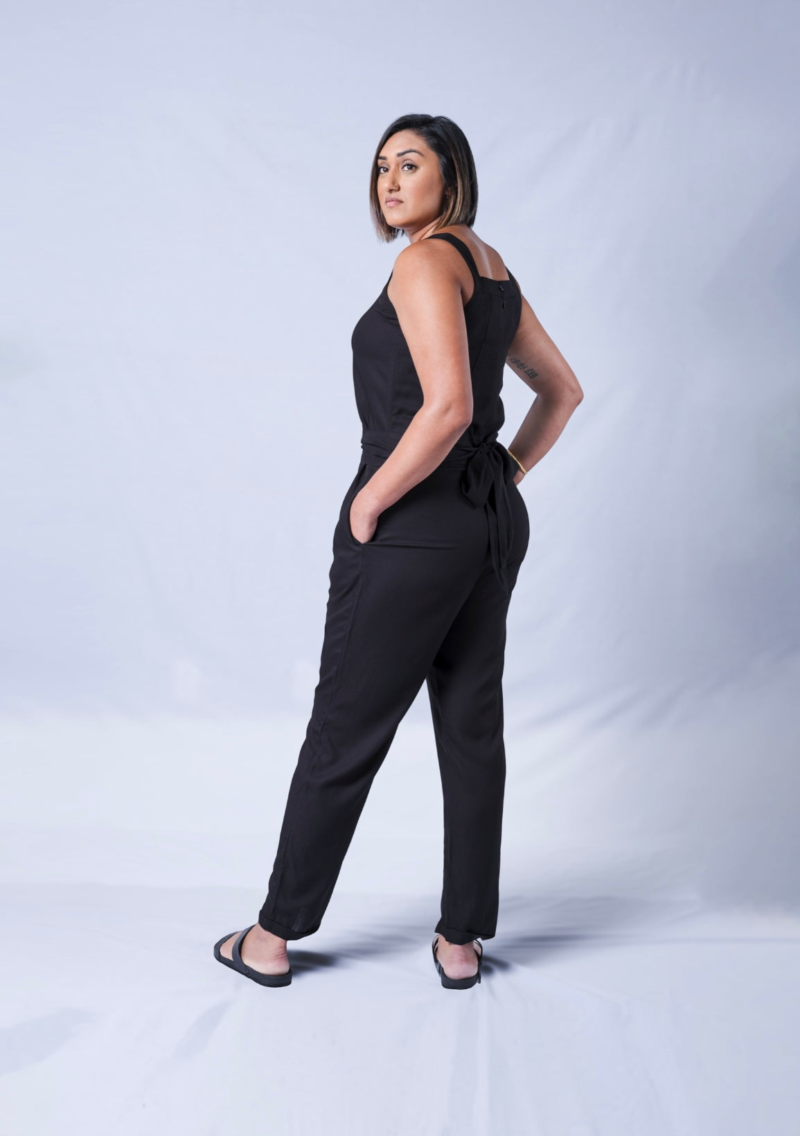 All In One Jumpsuit Model Standing to side showing side view. Waistband tied to back