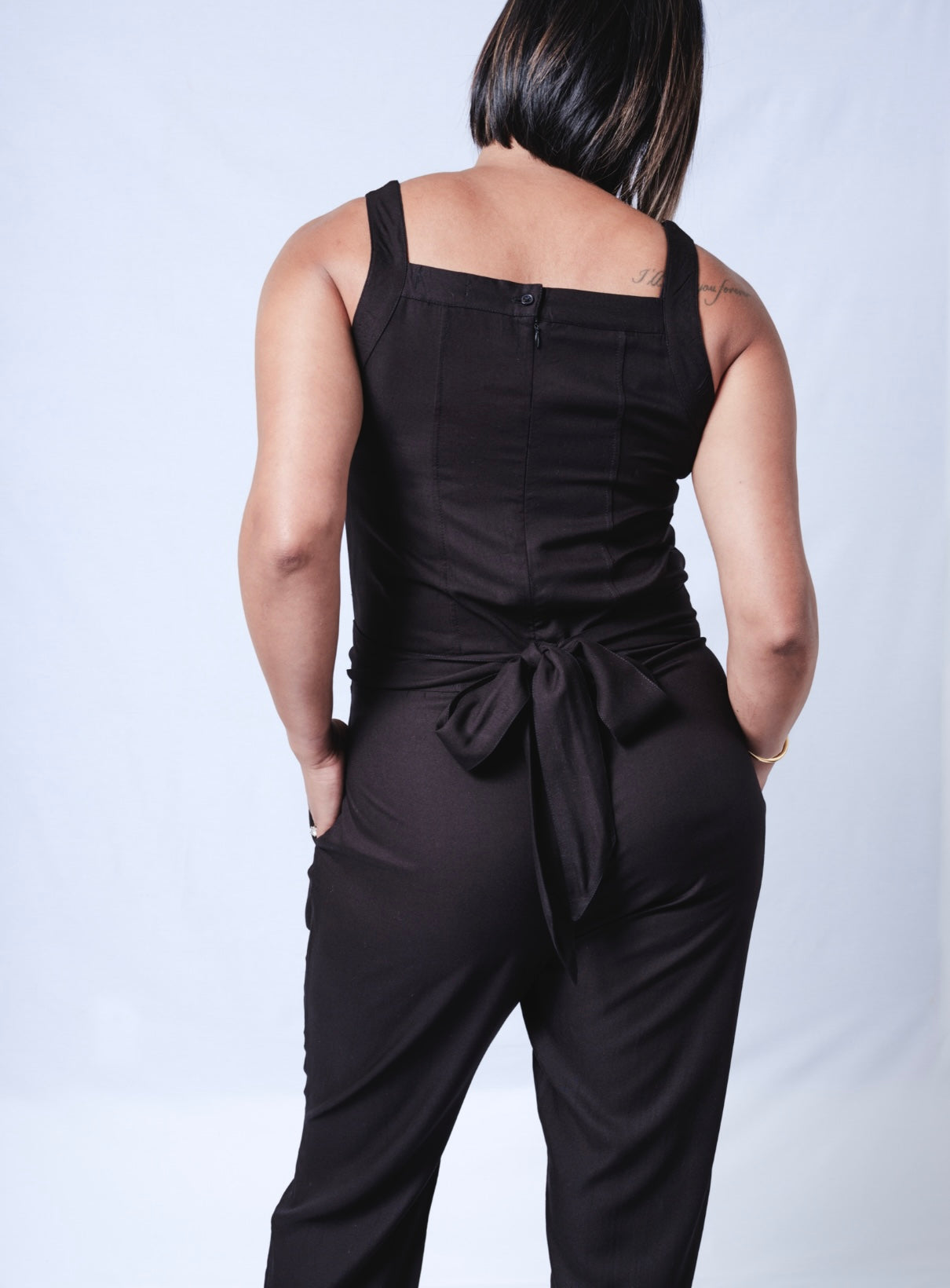 All In One Jumpsuit Model showing back of jumpsuit. Waistband tied to back and hands in pocket