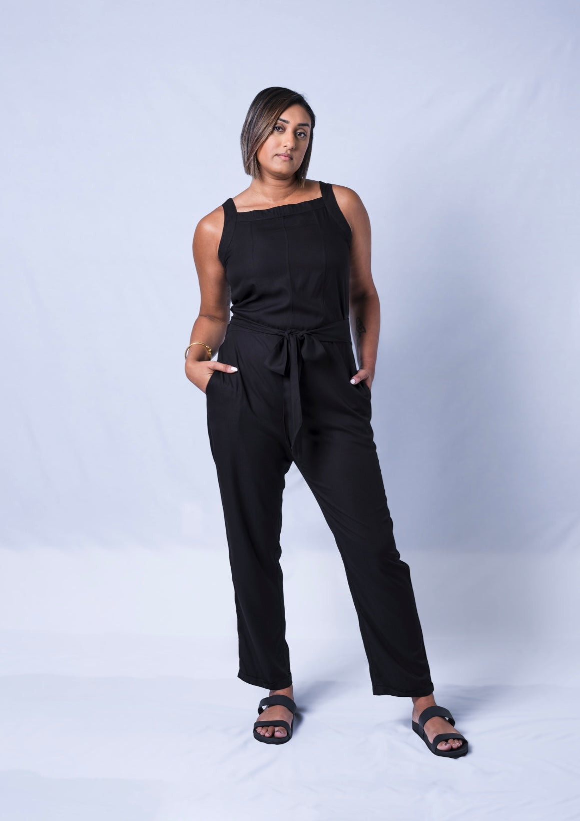 All In One Jumpsuit Model Standing showing front of the jumpsuit. Waistband tied to front and hands in pocket